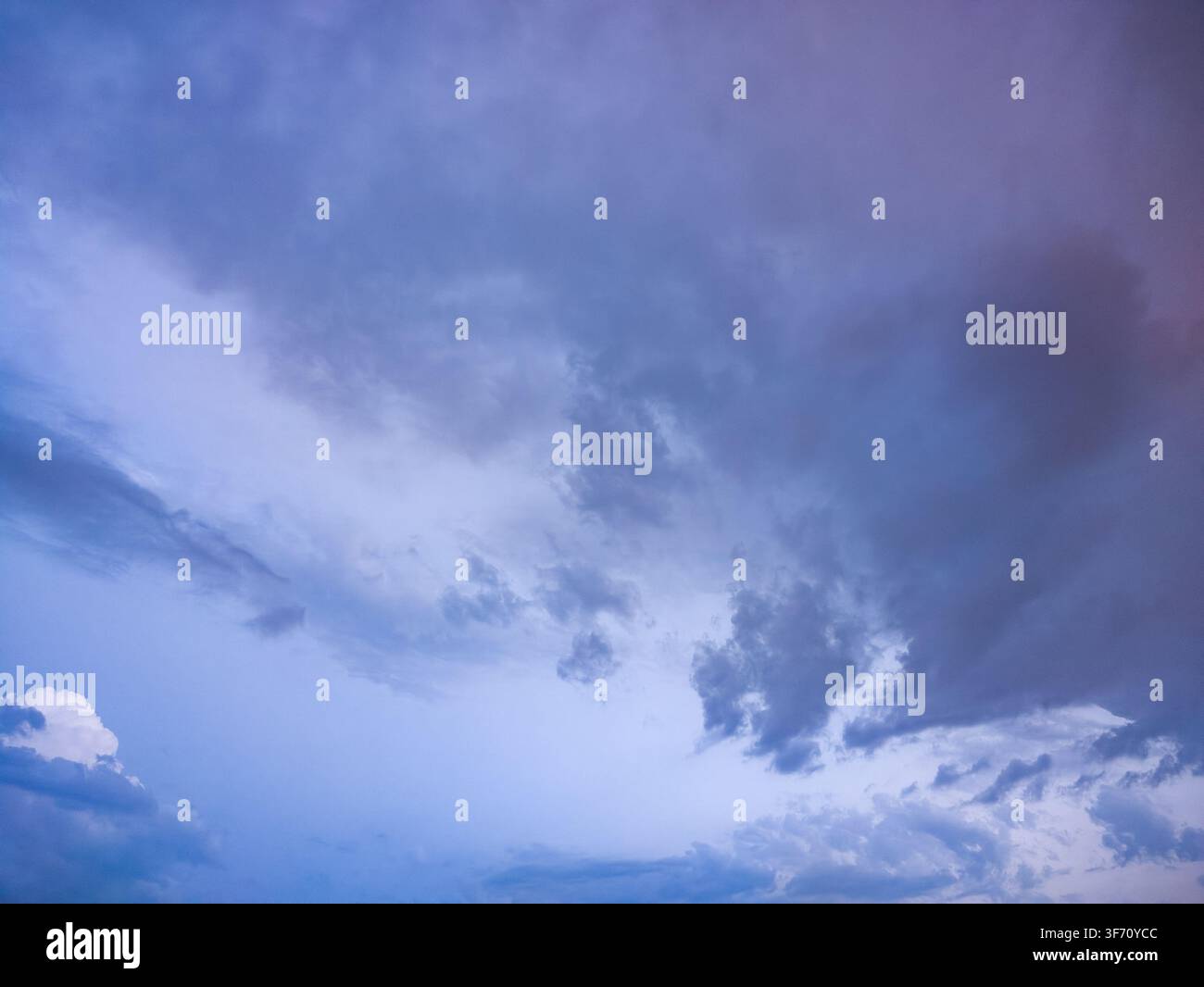 Cielo azzurro con nuvole sparse al crepuscolo. Nuvole più scure preannunciano tempo burrascoso. Toni viola morbidi riempiono l'orizzonte. Le nuvole si muovono lentamente nel cielo Foto Stock