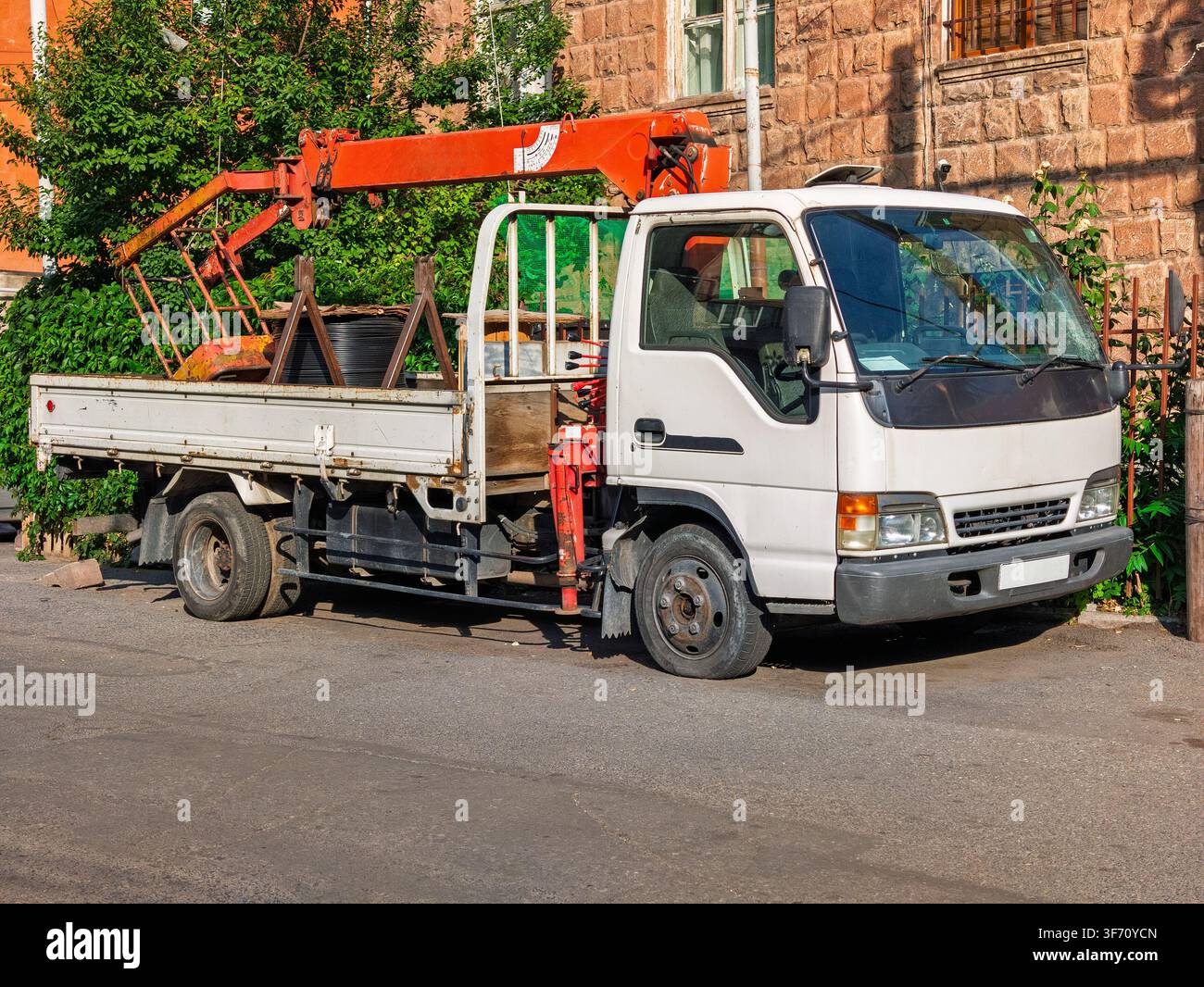 Camion bianco con gru arancione parcheggiato in strada. Il cassone del camion trasporta tronchi e attrezzature Foto Stock