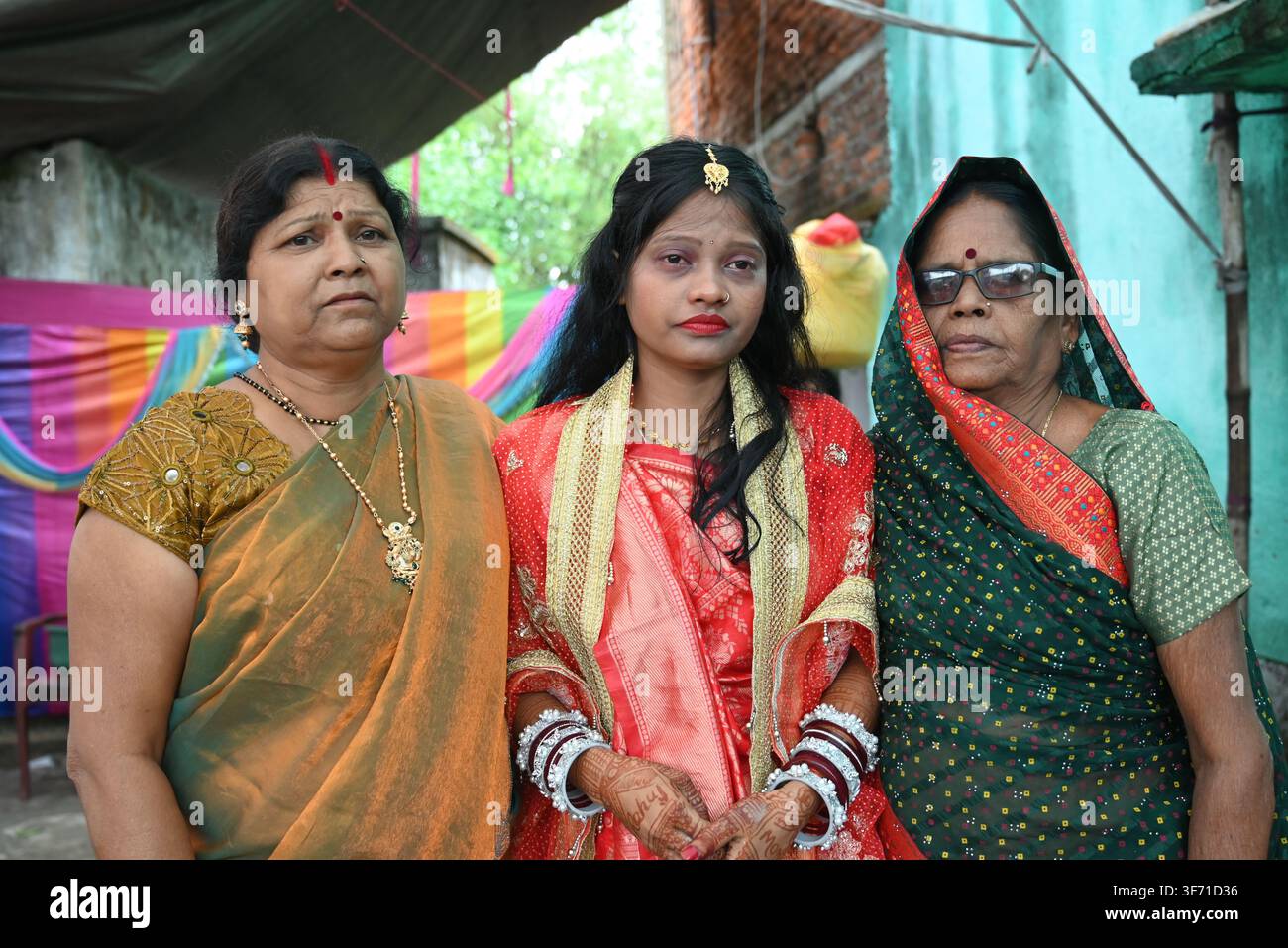 Sposa bengalese indiana in saree rosso in piedi con due donne anziane, membri della famiglia, durante la cerimonia nuziale nel Bengala Occidentale Foto Stock