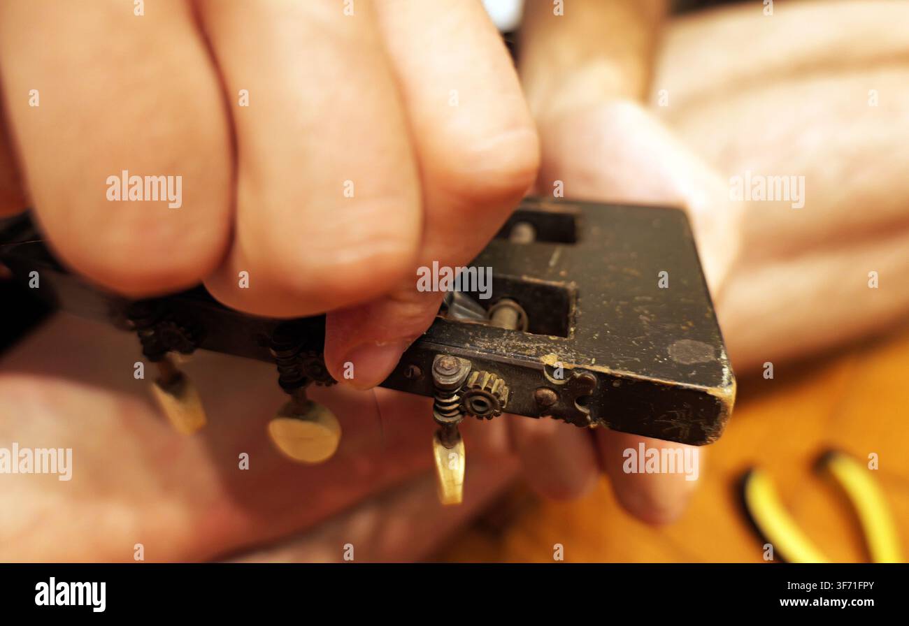 Mano che cura con attenzione una vecchia chitarra acustica, concentrandosi sul meccanismo intricato dei piroli e del capotasto, riflettendo l'artigianalità e Foto Stock