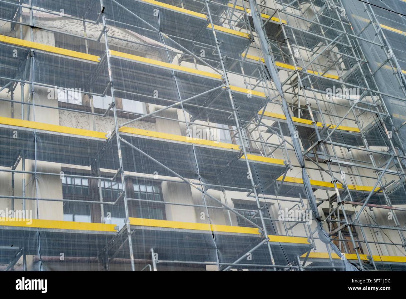 Struttura di impalcatura in tubi d'acciaio con pannelli gialli e rete protettiva installata contro l'esterno dell'edificio per la manutenzione della facciata commerciale Foto Stock