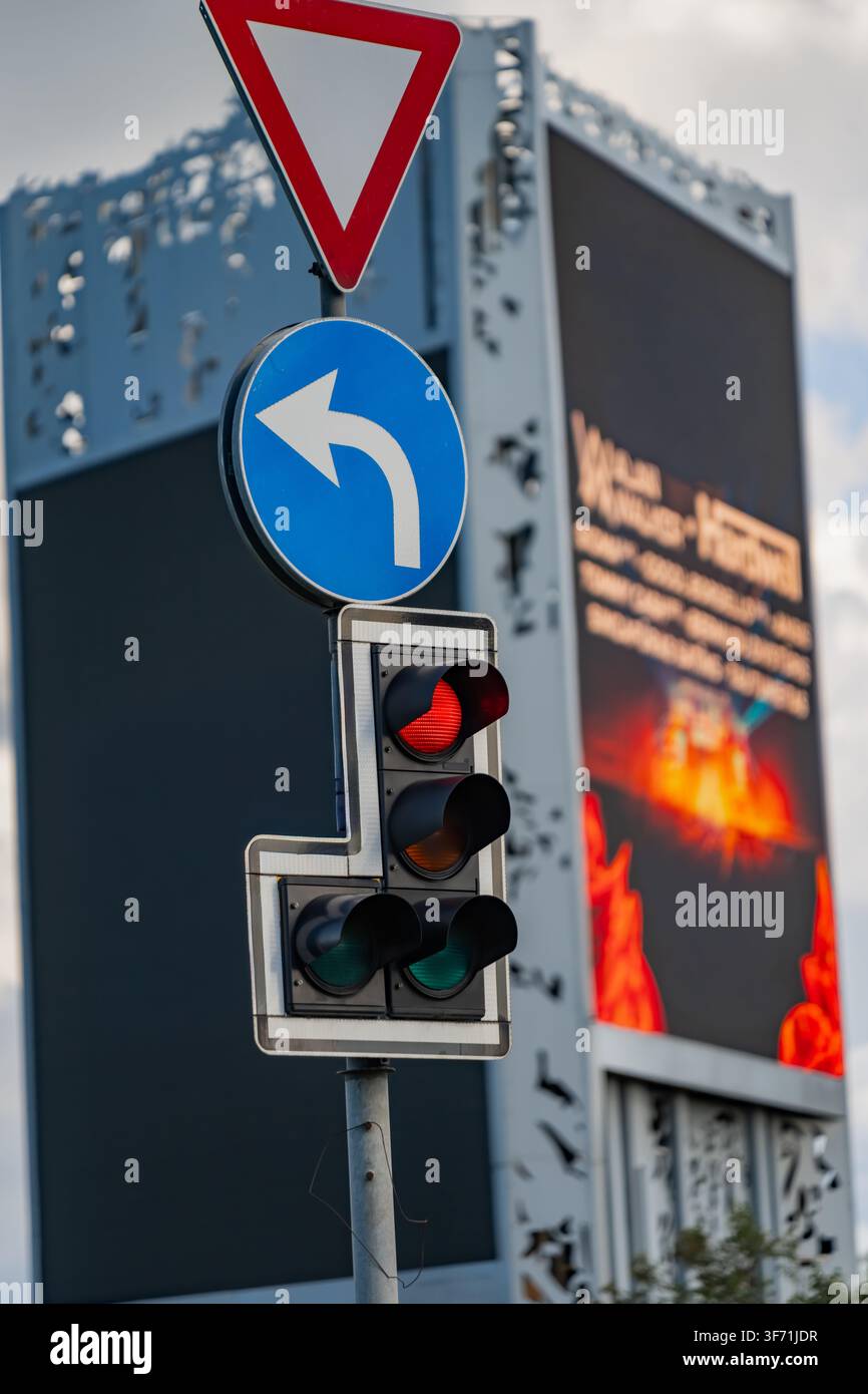 Testa del segnale di controllo del traffico che mostra luce rossa sotto il cartello di cedimento del passo e freccia direzionale circolare blu per la svolta a sinistra per la sicurezza stradale Foto Stock