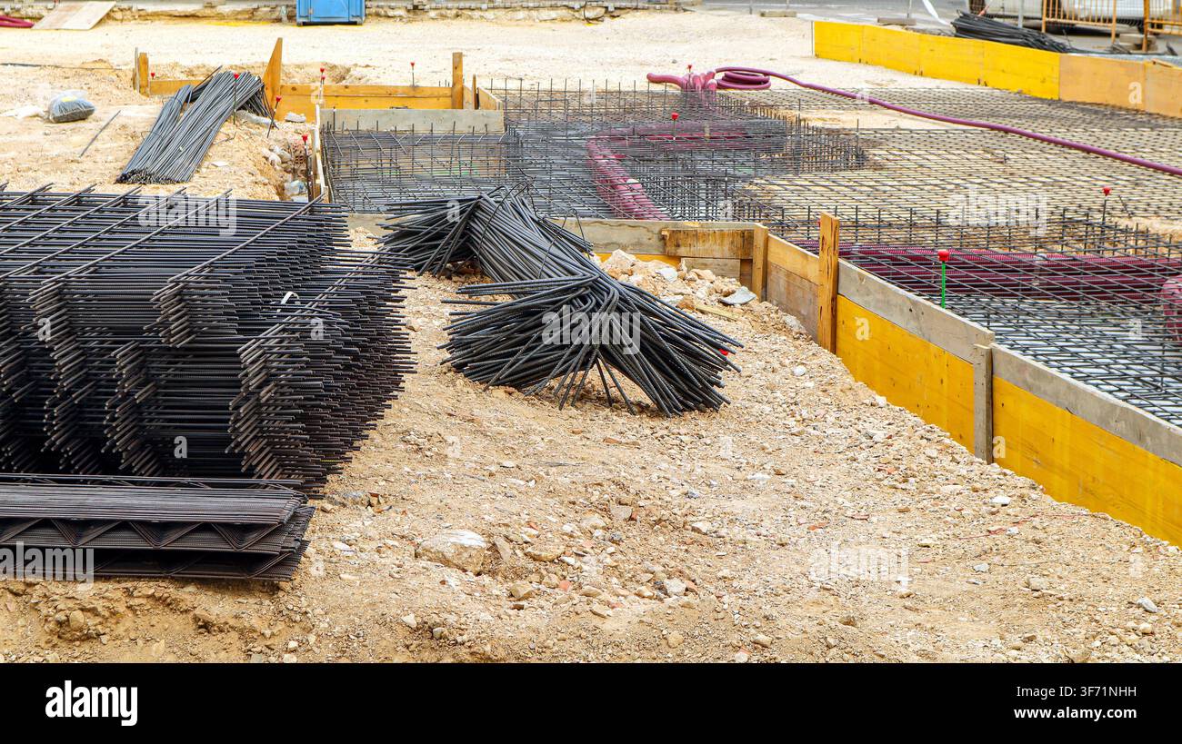Gli operai si preparano per la costruzione in un cantiere con barre d'acciaio e telai di legno. L'area è piena di materiali da costruzione e strumenti. Foto Stock