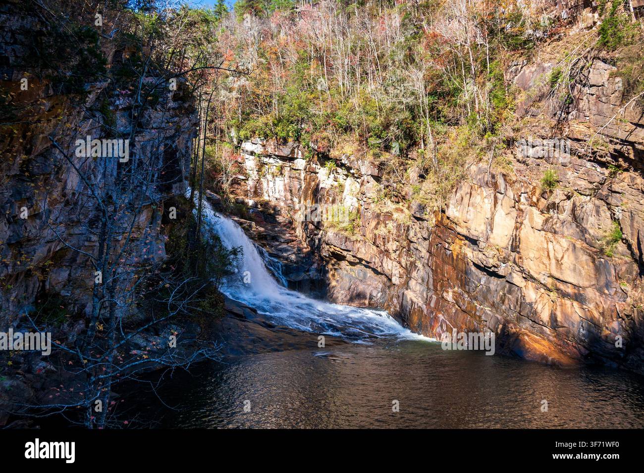 Una cascata si riversa su strati di scogliere rocciose in un bacino tranquillo alla base di un canyon boscoso in autunno. Foto Stock