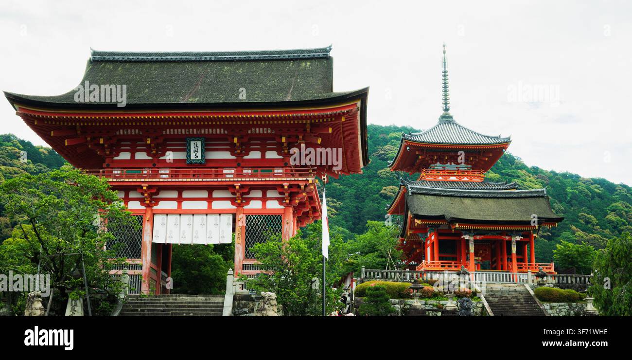 Il portale Nio-mon vermiglio e la pagoda adiacente a tre piani del tempio Kiyomizu-dera si ergono sopra una lussureggiante foresta collinare a Kyoto, in Giappone. Foto Stock