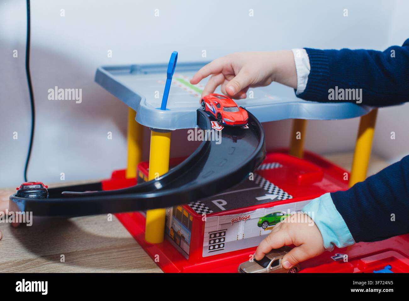 Un bambino gioca con macchinine in miniatura su un binario di parcheggio in plastica a più livelli al chiuso. Foto Stock