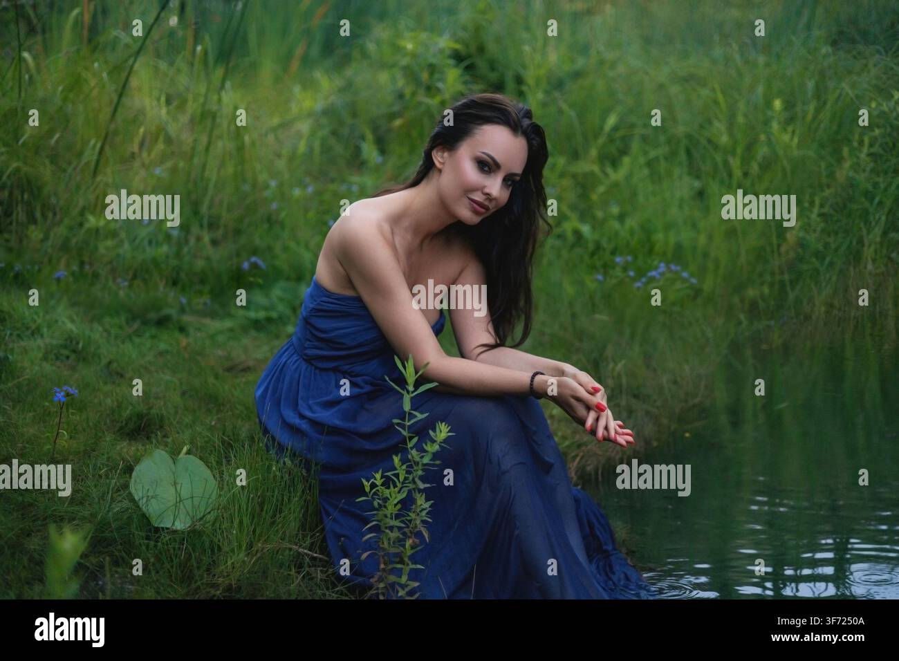 Una bella giovane donna in abito posa sull'erba verde. Concetto fiabesco ed estetico. Foto Stock