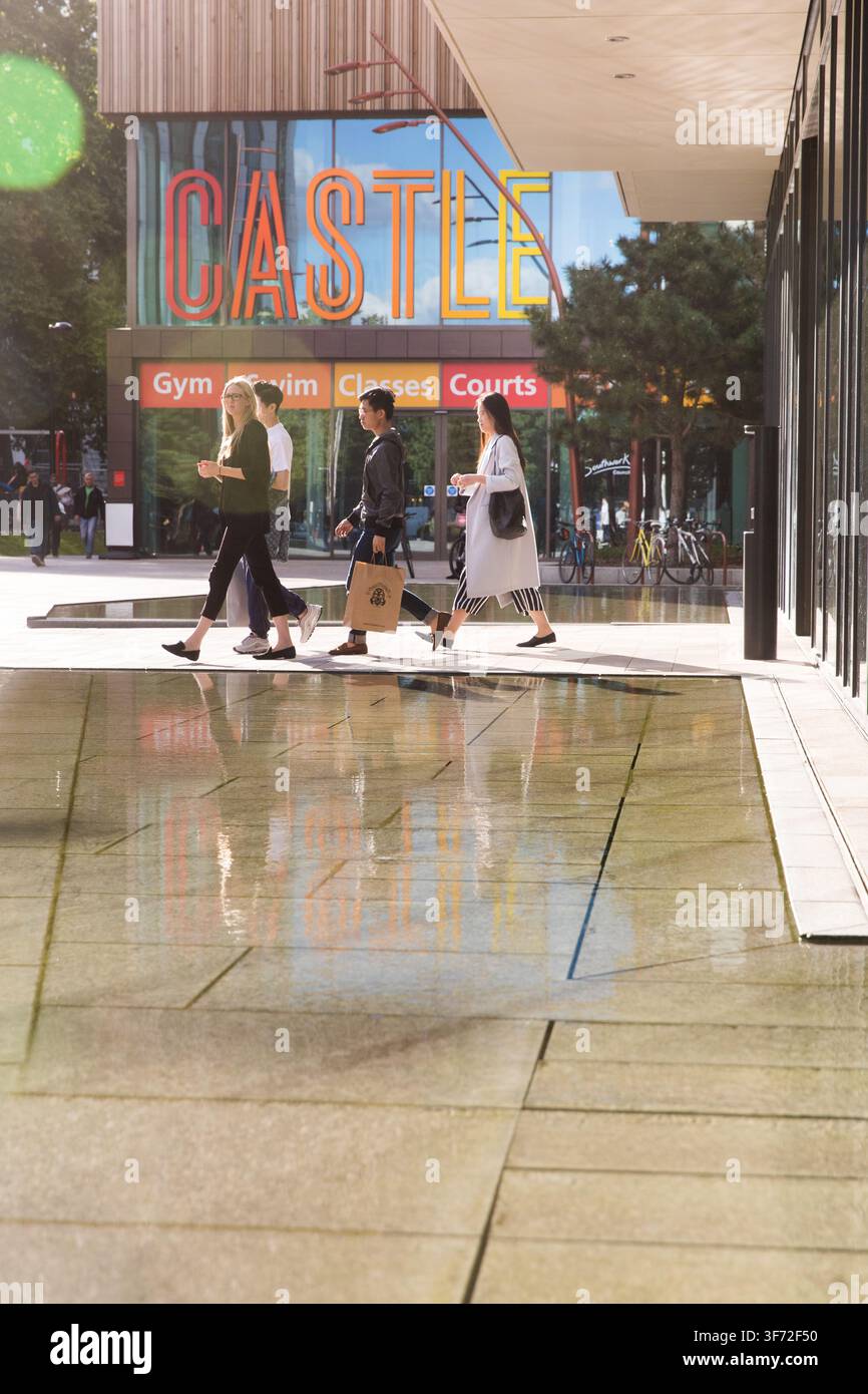 I pedoni passano davanti al The Castle Centre a Elephant and Castle, Londra, riflettendosi nella piscina moderna del cortile in un pomeriggio soleggiato. Foto Stock