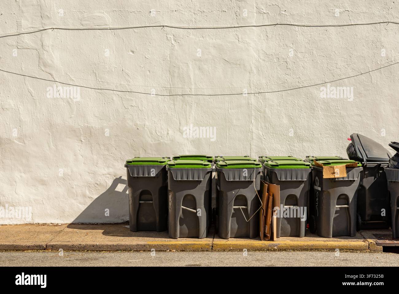 Una fila di bidoni della spazzatura e della raccolta differenziata contro un muro consumato nel centro di Phoenixville, Pennsylvania, con ampio spazio per il testo e un paesaggio urbano stradale s Foto Stock