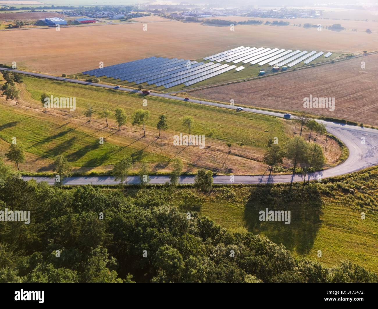 Vista aerea di una fattoria solare con file di pannelli fotovoltaici situati in un paesaggio rurale con una strada tortuosa, alberi e campi a Viglas, Banska By Foto Stock