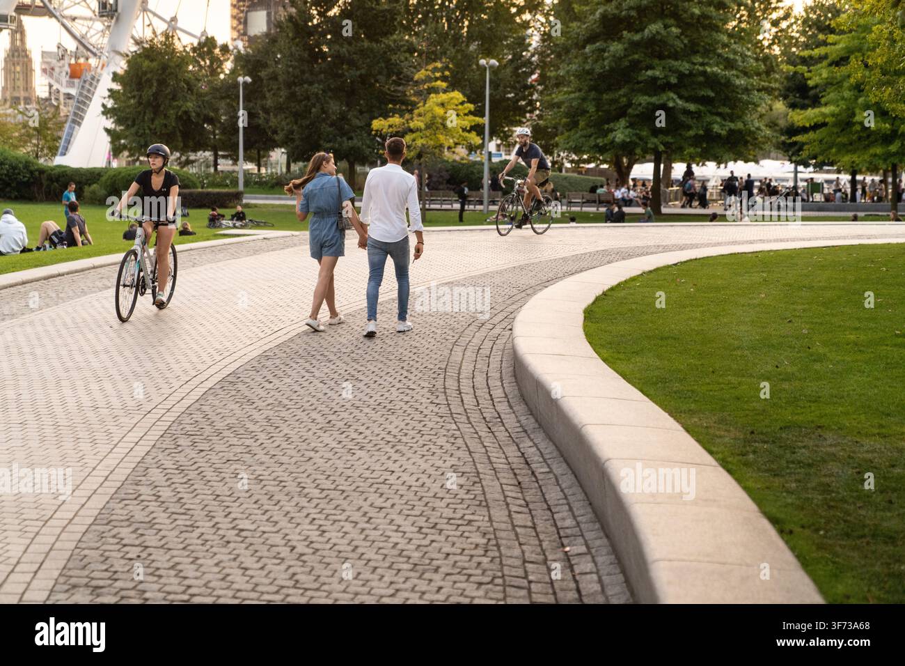 I visitatori camminano e pedalano attraverso i Jubilee Gardens di Londra, godendosi una piacevole giornata accanto all'iconico London Eye. Foto Stock