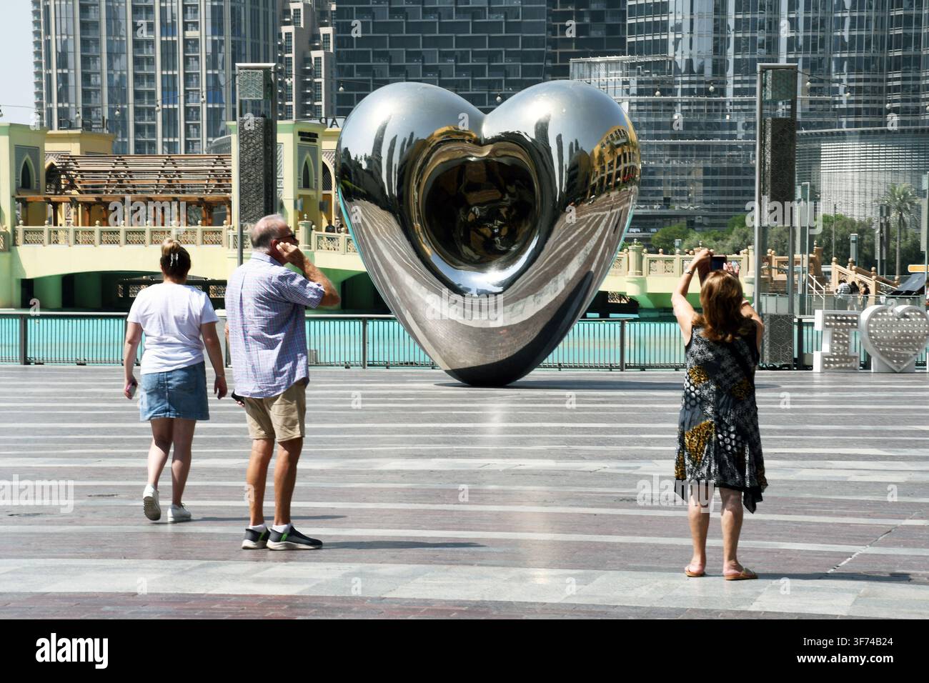 tre turisti alla scultura a forma di cuore in cromo fuori dal Dubai Mall Foto Stock