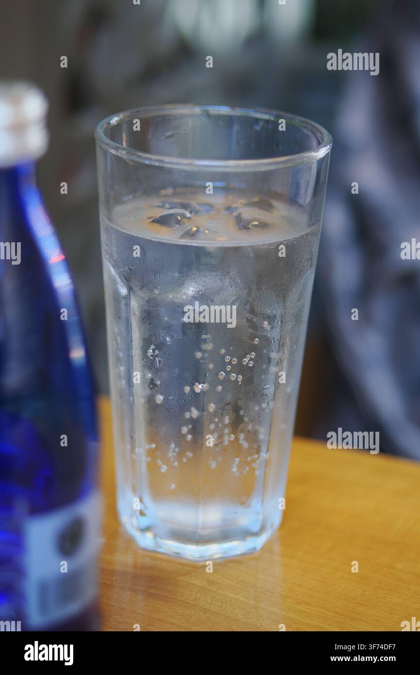 Un bicchiere di acqua frizzante o bevanda gassata servita con bolle di ghiaccio visibili in un tumbler sfaccettato su un tavolo di legno Foto Stock