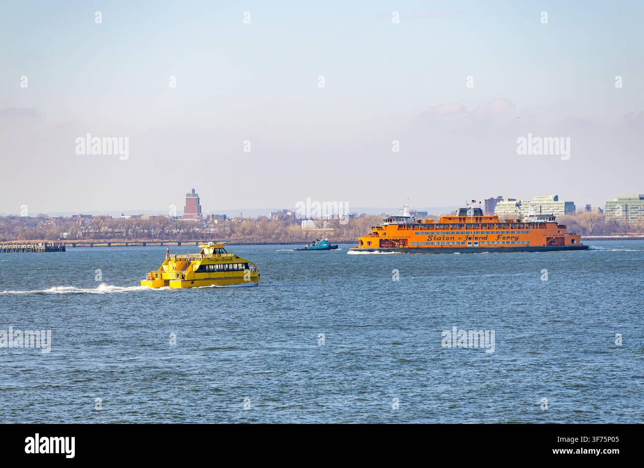 New York, USA - 20 febbraio 2026: famoso battello arancione del Staten Island Ferry che naviga con una nave taxi gialla sulle acque del porto di New York Foto Stock