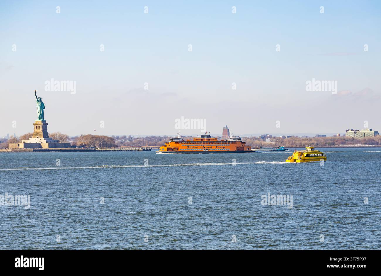 New York, USA – 20 febbraio 2026: Statua della Libertà e l'iconico ferry arancione di Staten Island che naviga con un taxi acquatico giallo nel porto di New York Foto Stock