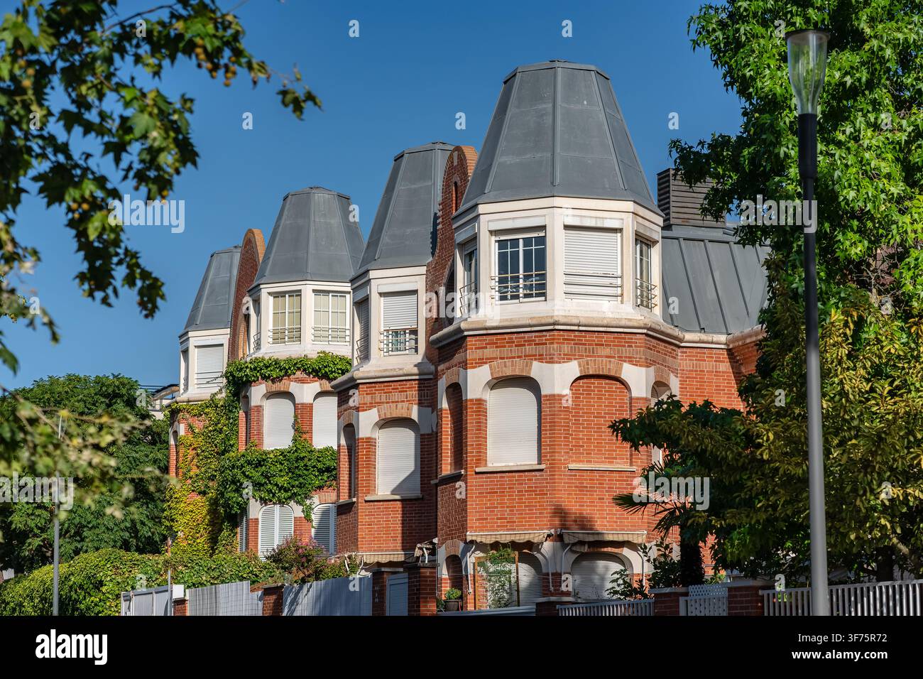 Filiera di edifici residenziali in mattoni rossi con tetti mansardati grigi incorniciati da alberi verdi maturi Foto Stock