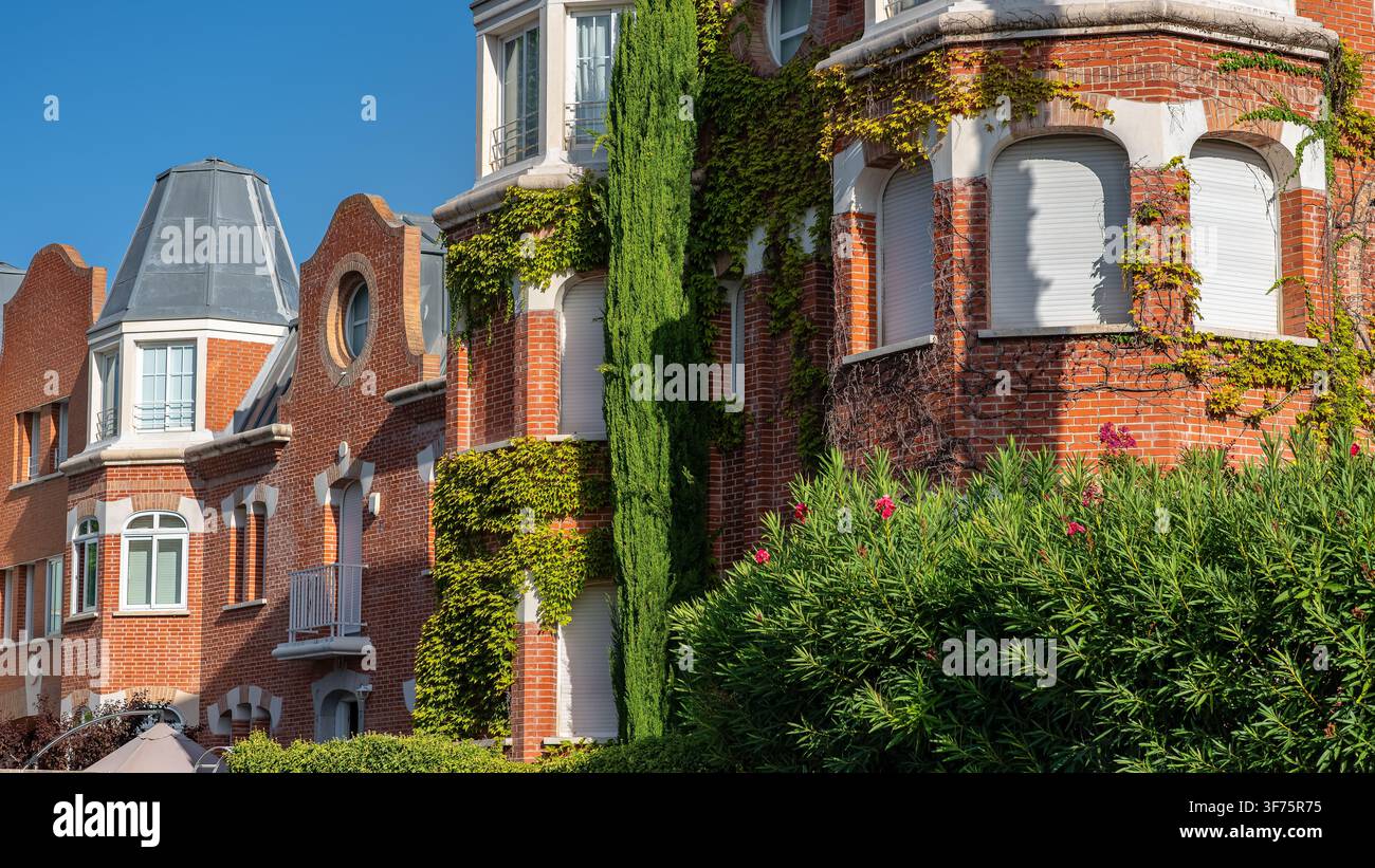 Residenza in mattoni rossi illuminata dal sole con abbaini a mansarda con finestre ad arco e edera rampicante verde fitta Foto Stock