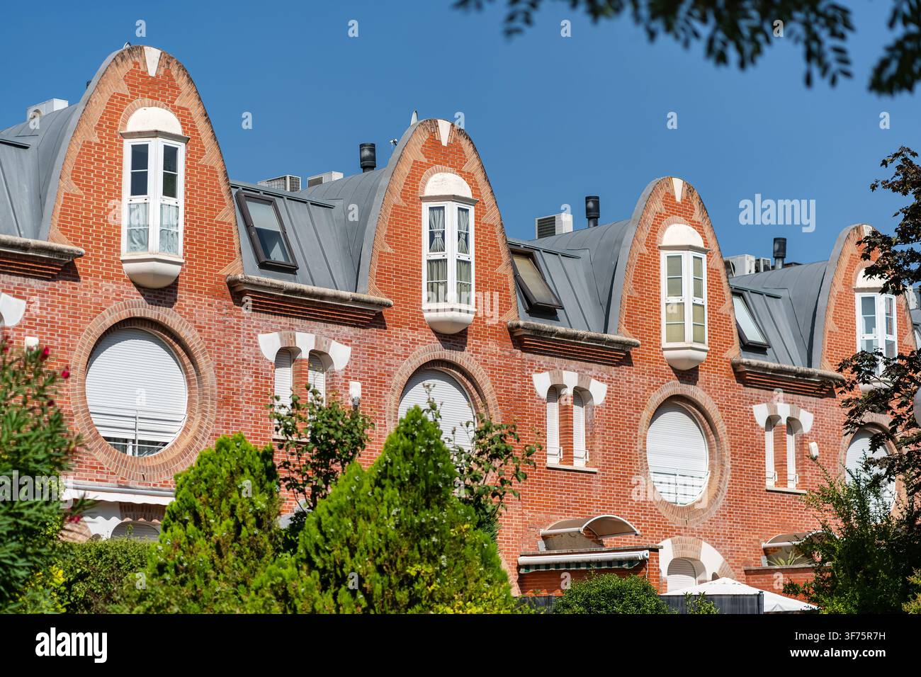 Gabbie di mattoni curvi ripetuti e finestre circolari su un elegante edificio residenziale illuminato dal sole Foto Stock