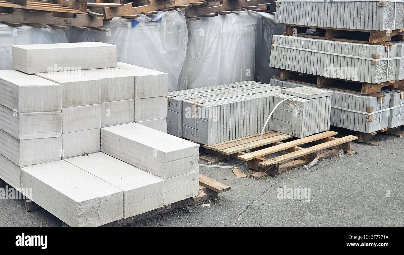 Vista frontale di blocchi di cemento grigi impilati (blocchi di scoria) e di materiali da costruzione imballati su bancali di legno, ideali per la muratura, la costruzione di pareti e Foto Stock