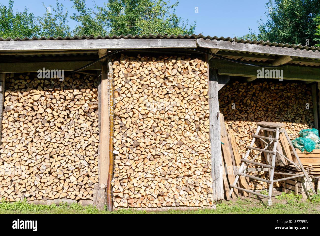 Ampia veduta di una legnaia di campagna completamente rifornita di legna da ardere accuratamente tagliata e impilata per il riscaldamento invernale. Foto Stock