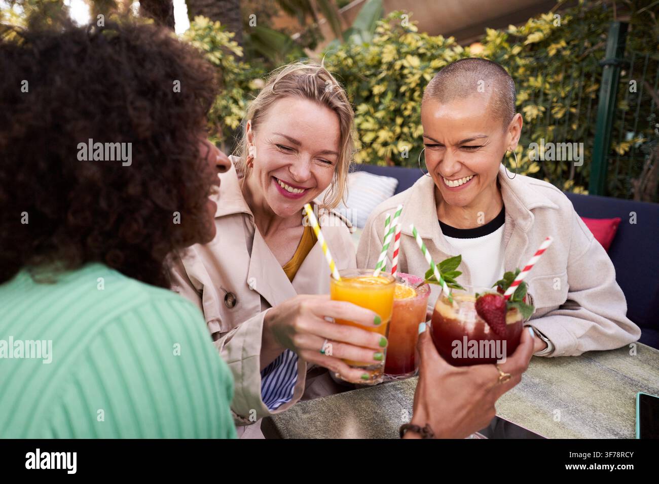 Tre donne mature allegre bevono all'aperto in terrazza, brinda con cocktail o mocktail Foto Stock