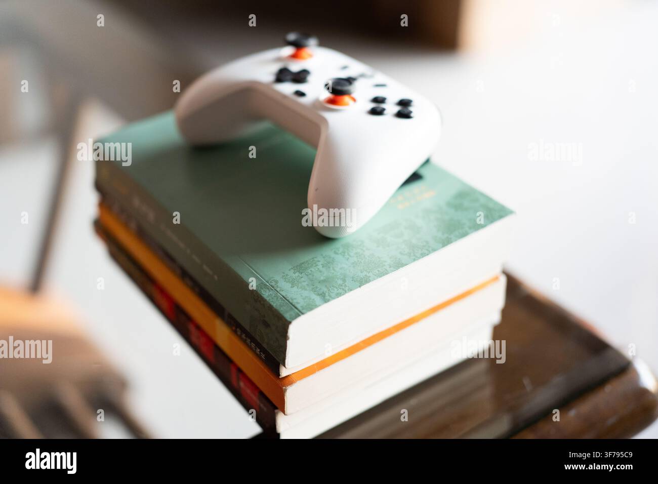 Controller Google Stadia bianco appoggiato su una pila di libri con dorsi verdi e arancioni, messa a fuoco morbida Foto Stock