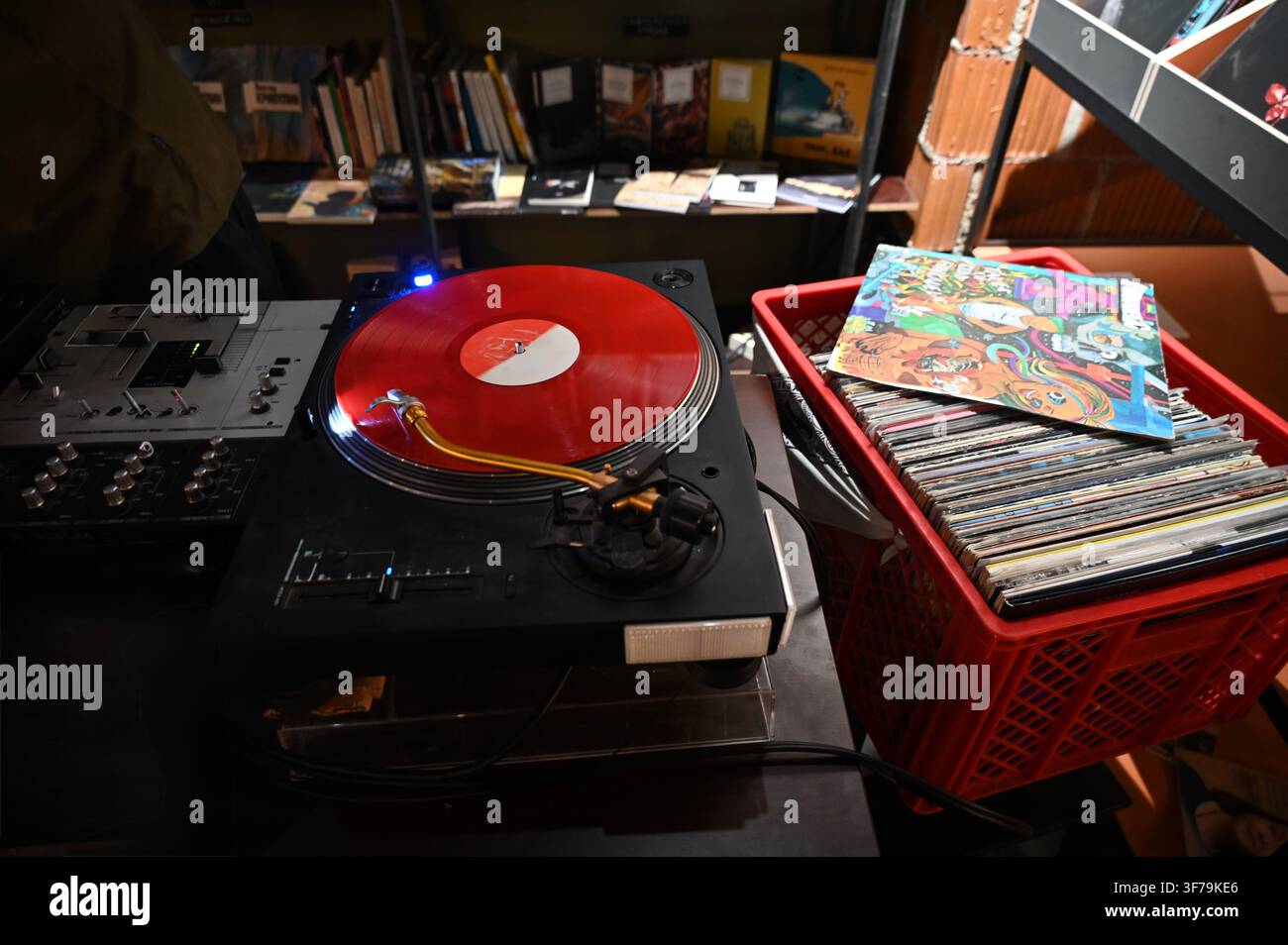 Una fotografia orizzontale che cattura un giradischi DJ che suona un vinile rosso vivace, con una cassa rossa piena di dischi e copertine posizionata accanto su un tavolo in un negozio di dischi. Foto Stock