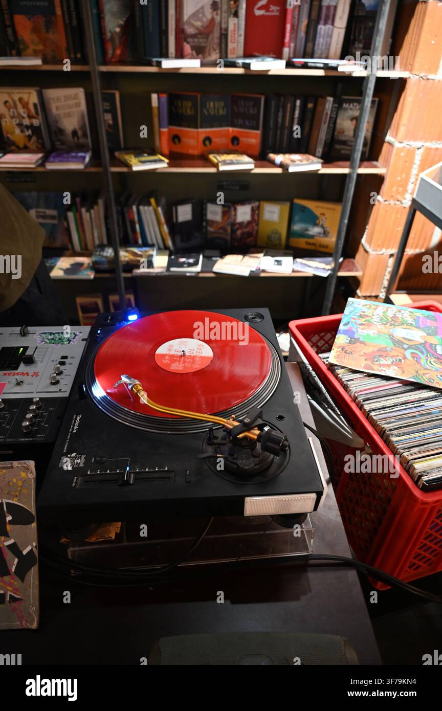 Una fotografia orizzontale che cattura un giradischi DJ che suona un vinile rosso vivace, con una cassa rossa piena di dischi e copertine posizionata accanto su un tavolo in un negozio di dischi. Foto Stock