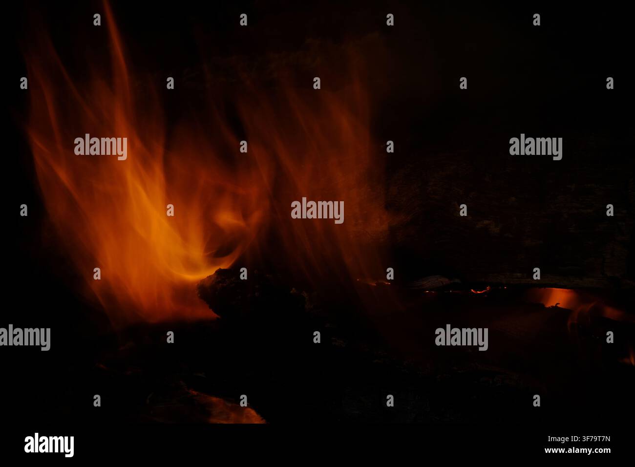 Fuoco fiammeggiante, un ceppo che brucia in un camino, fuoco arancione, sfondo nero Foto Stock