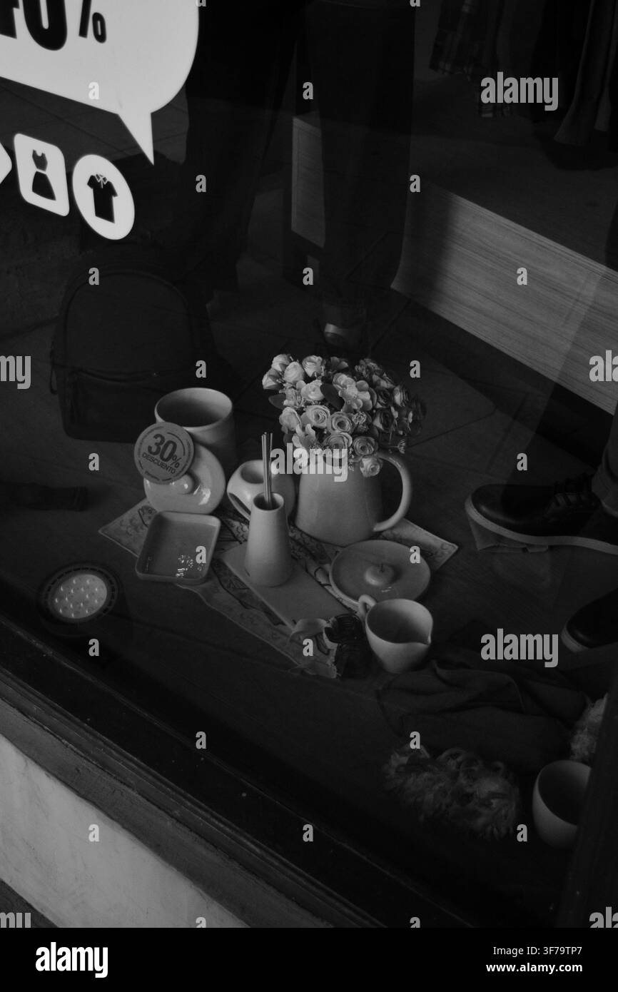 Foto di strada in bianco e nero di un tavolo da caffè accogliente con fiori riflessi attraverso la vetrina del negozio. Foto Stock
