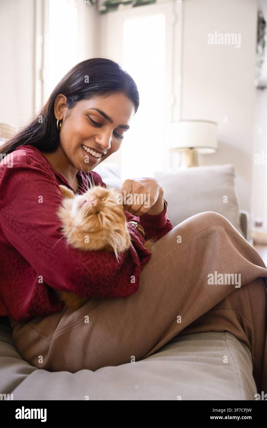 Donna sorridente che coccola un gatto sul divano a casa Foto Stock