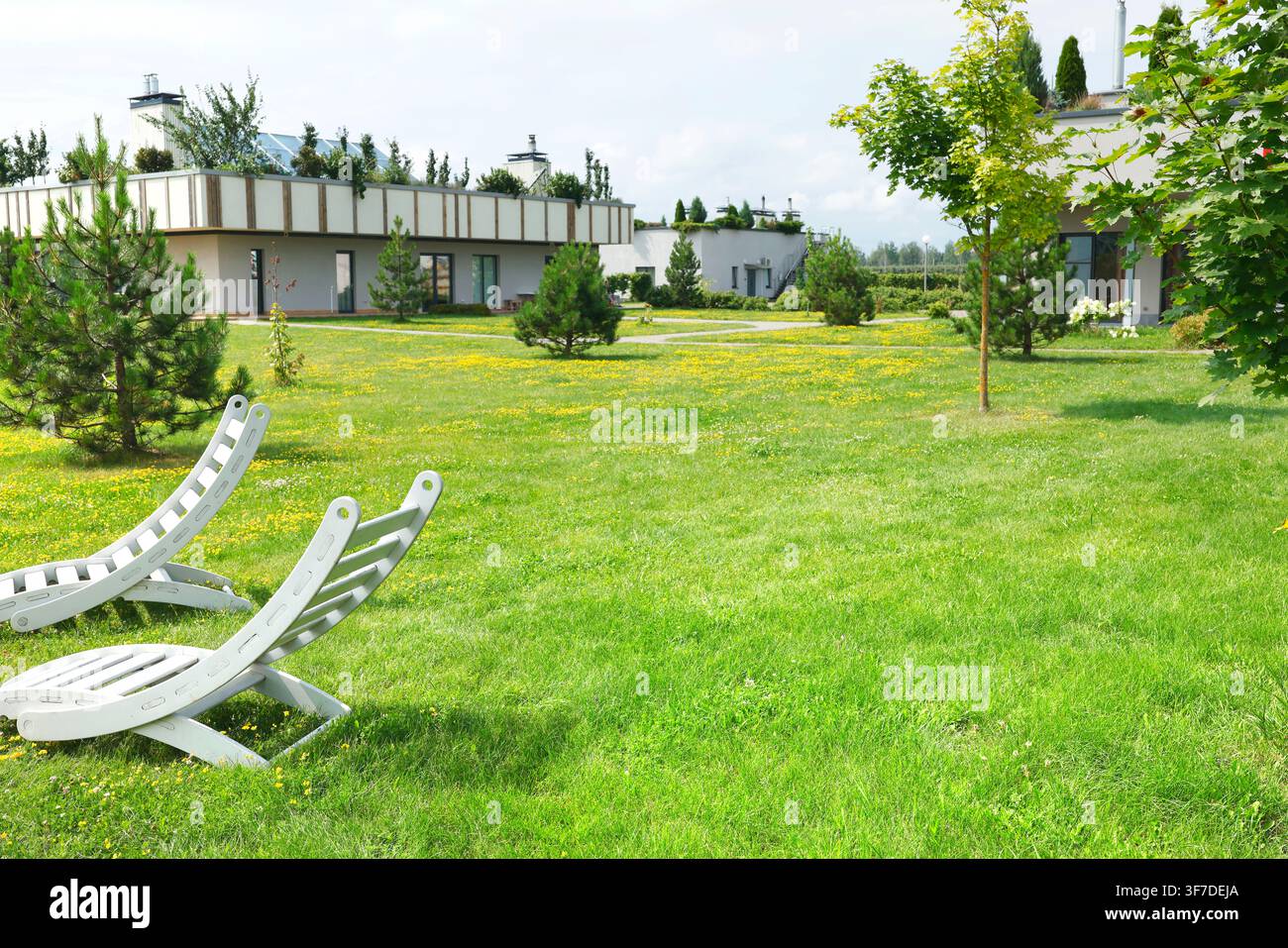 Zona di relax all'aperto premium con chaise longue bianche su un prato verde rigoglioso. Proprietà immobiliare di lusso in una moderna residenza suburbana ecologica Foto Stock