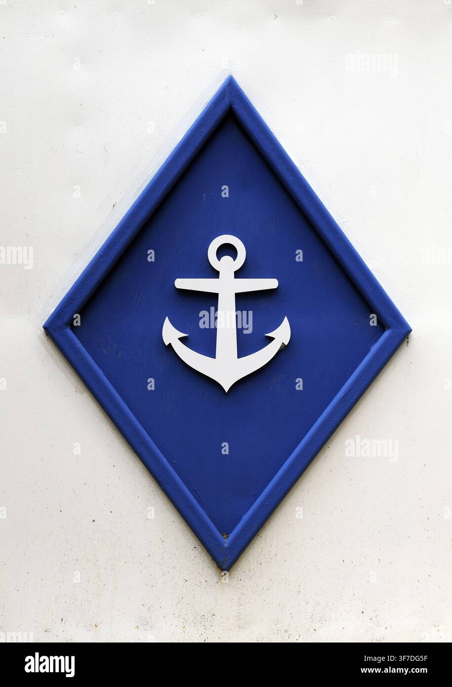 Simbolo di ancora bianca che appare su un cartello marittimo a forma di rombo blu, che rappresenta temi nautici, stabilità e navigazione, montato su un w ruvido Foto Stock