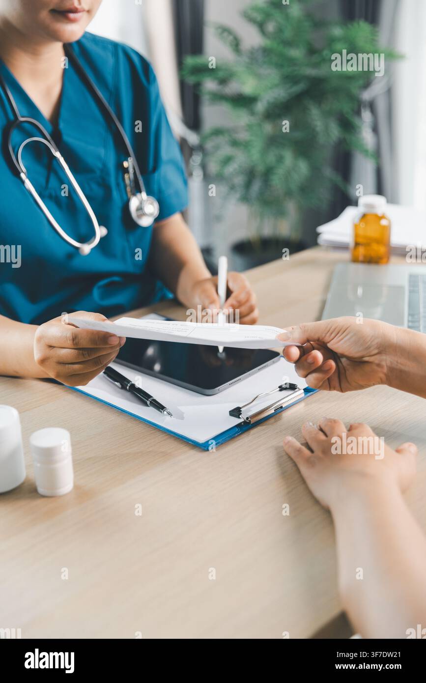 Medico che consegna un foglio di prescrizione al paziente durante la consultazione in clinica con flaconi di medicinali sul tavolo, documento sanitario, farmacia, farmaci e Foto Stock
