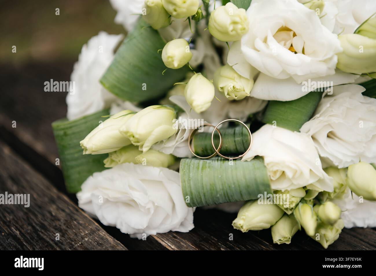 Due anelli nuziali d'oro su un mazzo bianco di fiori di eustoma su un tavolo di legno Foto Stock