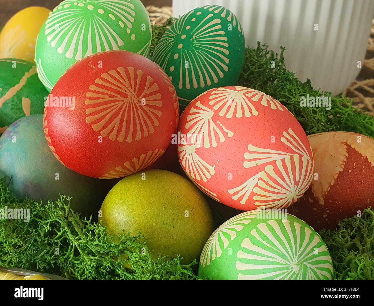 Una composizione ravvicinata di uova di Pasqua colorate dipinte a mano, esposte su muschio verde. Le uova presentano vari colori tra cui rosso acceso, corallo Foto Stock