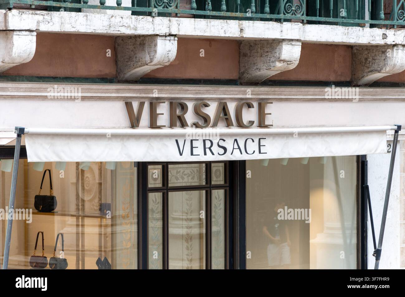 ITALIA, VENEZIA, 11 LUGLIO 2025: Una facciata del negozio Versace con tenda bianca, grande insegna e borse esposte nella vetrina è mostrata sotto un b ornato Foto Stock