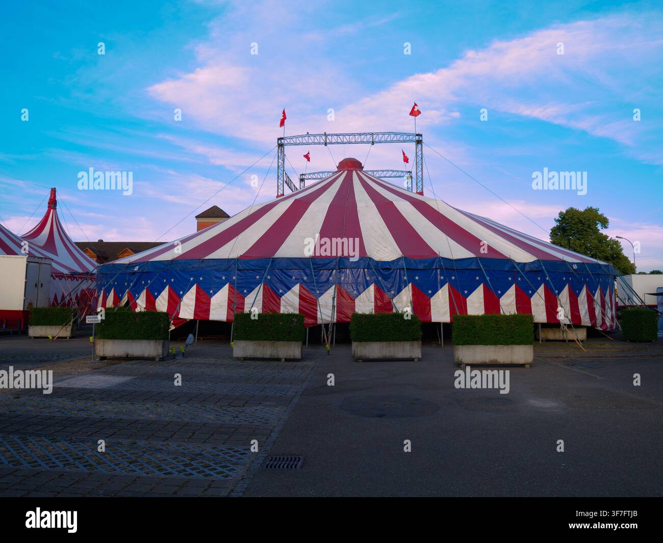 Grande tenda da circo tradizionale con tela rossa e bianca installata sull'asfalto durante le attività di trasferimento Foto Stock
