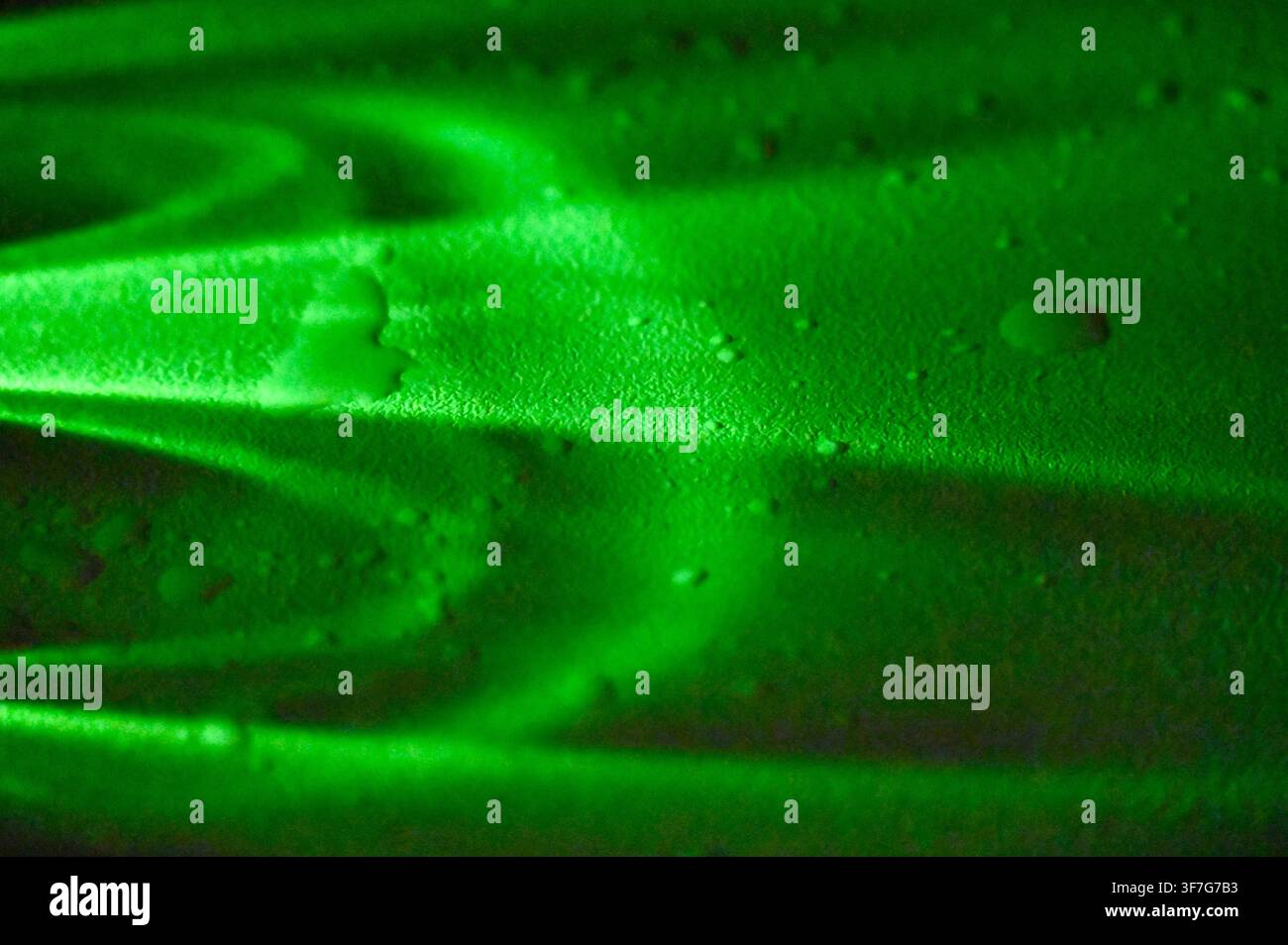 Fotografia macro commerciale che si concentra sulla texture specifica di un moderno piano da tavolo verde opaco, coperto casualmente da gocce di rugiada o acqua trasparenti. L'illuminazione laterale drammatica enfatizza la qualità tattile della superficie. Ideale per concetti di design d'interni, cataloghi di mobili, biblioteche di materiali di superficie e pubblicità di prodotti per la pulizia o l'idratazione. Foto Stock