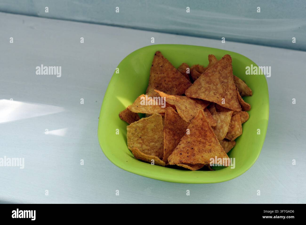 Chips di tortilla che riempiono una ciotola verde brillante, offrendo un'opzione di snack croccante e saporito, pronti per essere intinti o serviti come antipasto Foto Stock