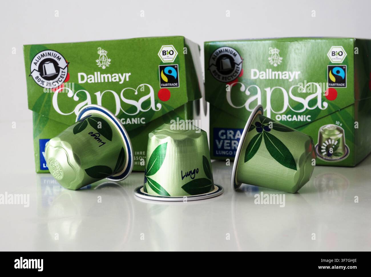 Germania, Bavaria - 9 agosto 2026: Capsule di caffè organico Dallmayr capsa verdi disposte davanti a due scatole di caffè verdi su una superficie riflettente bianca Foto Stock