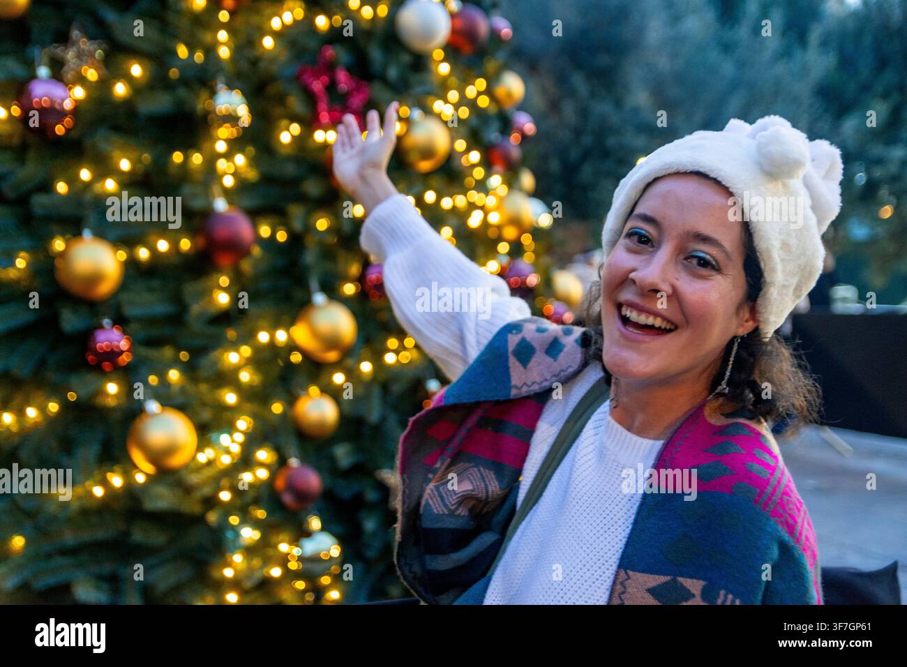 Donna allegra che celebra la stagione delle festività vicino a un albero di Natale illuminato Foto Stock