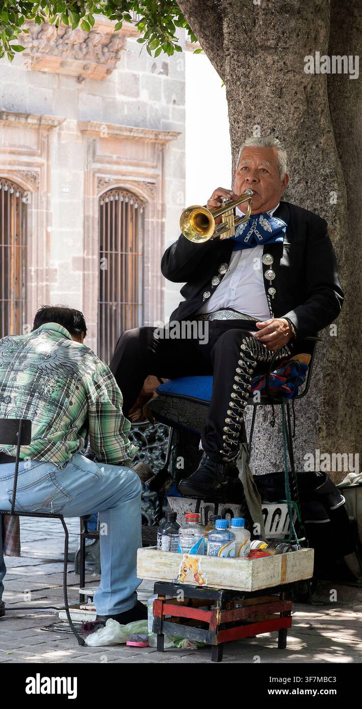 Musicista di strada mariachi che suona la tromba mentre si fa lucidare le scarpe sotto un albero a San Miguel de Allende, Messico Foto Stock
