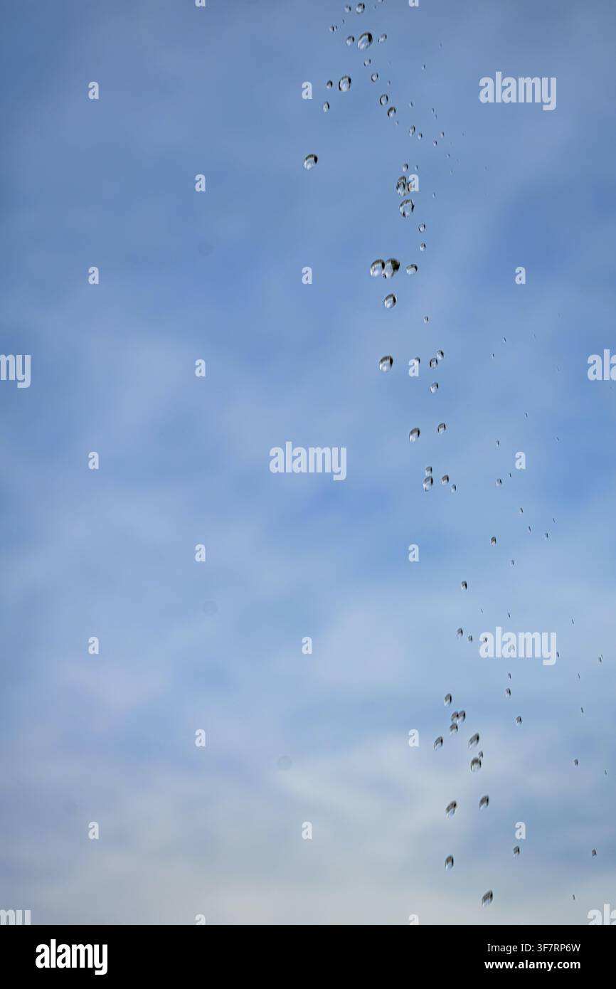 Goccioline cascano su un cielo blu brillante. Le nuvole si muovono dolcemente sullo sfondo. Ogni goccia luccica alla luce del sole. Un momento tranquillo della natura catturato a metà Foto Stock