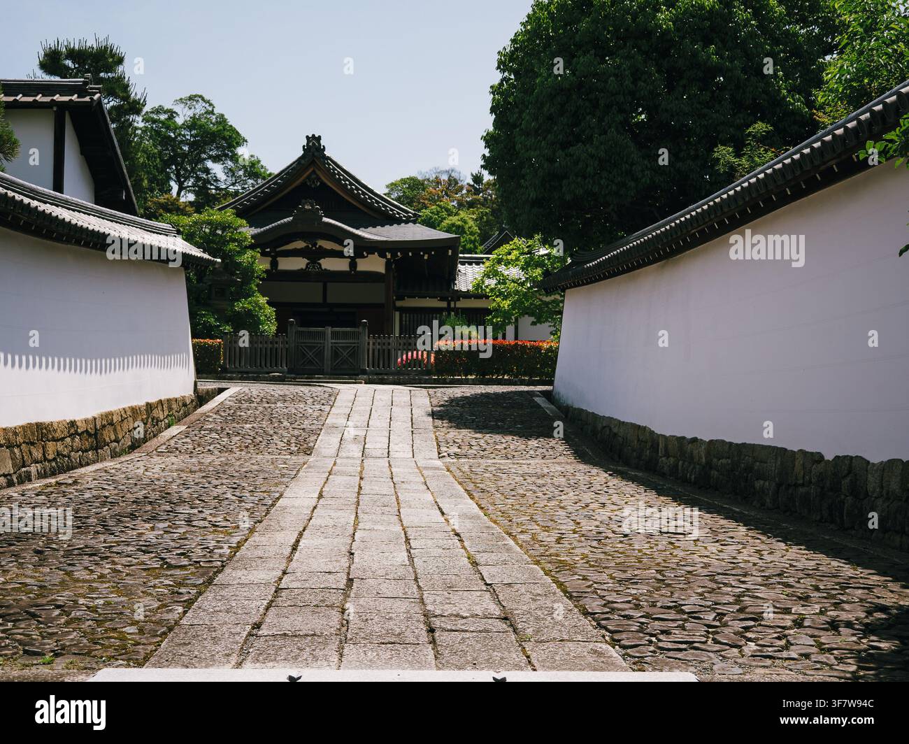 Sentiero lastricato di pietra tra complessi di templi dalle pareti bianche che conduce a un cancello di legno a Kyoto, Giappone Foto Stock
