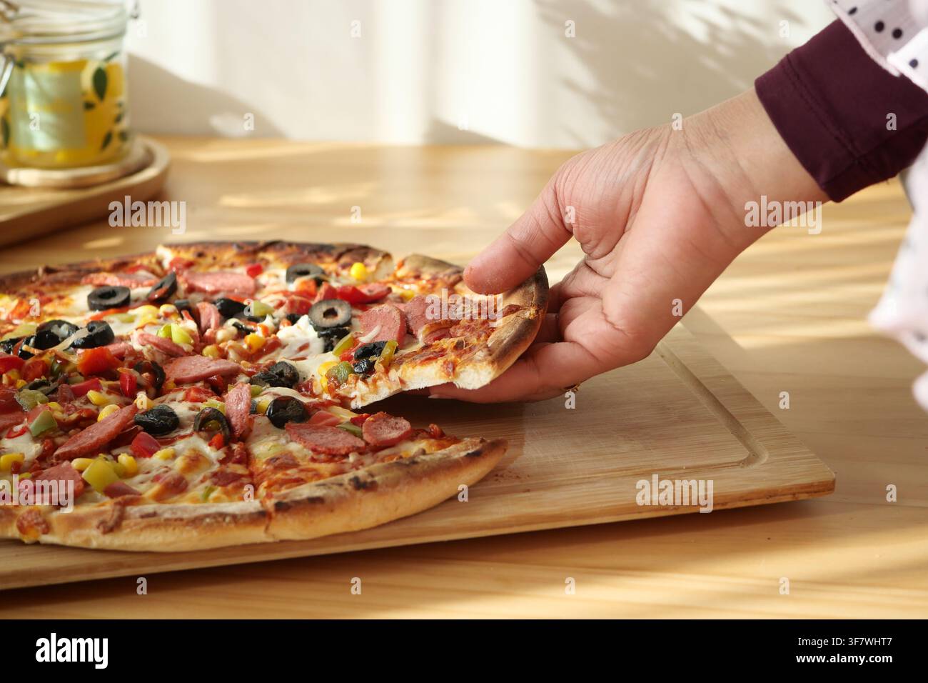 Persona che prende una fetta di pizza da un tavolo di legno Foto Stock