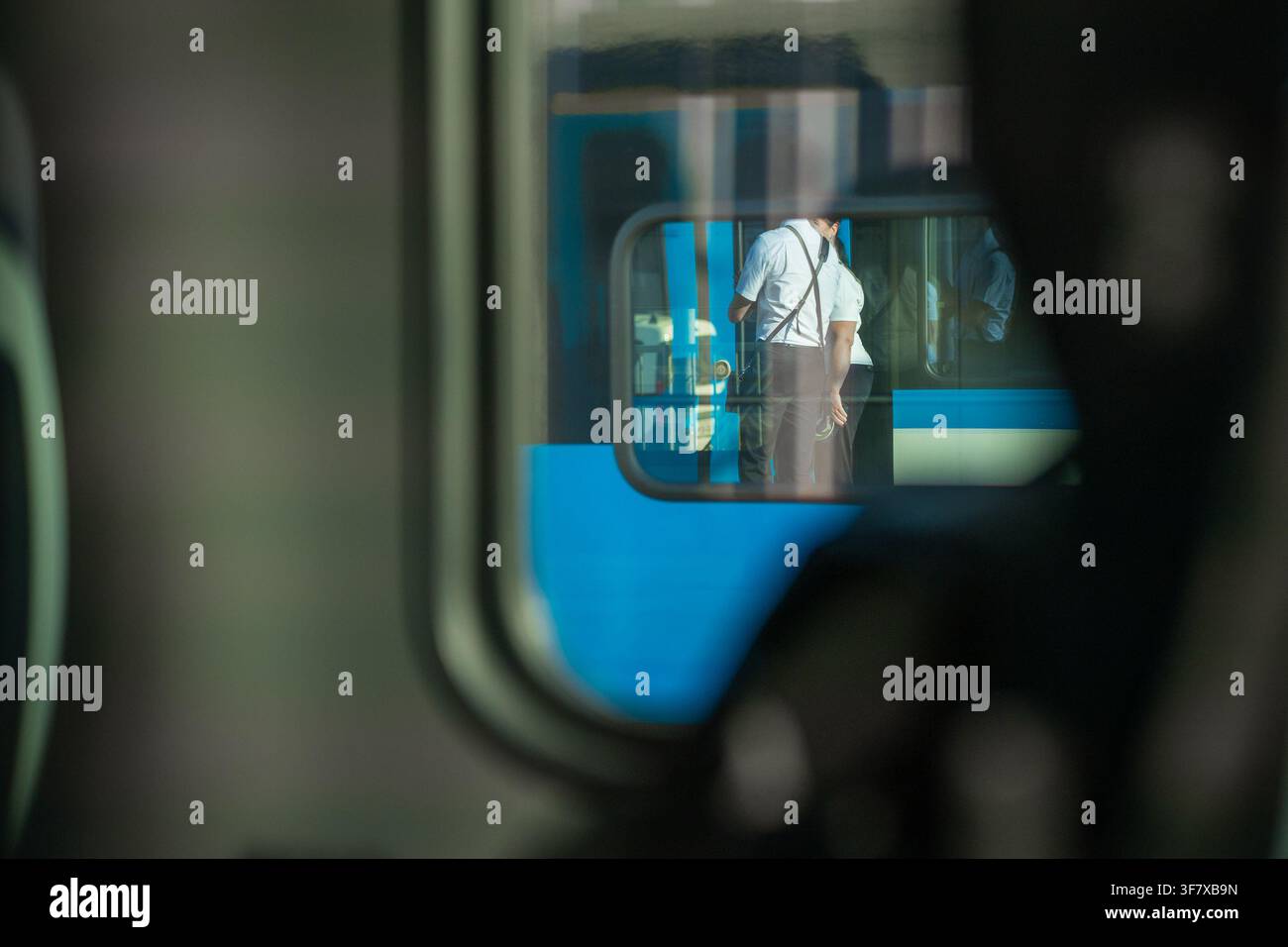 Un riflesso in un finestrino del treno mostra personale ferroviario in uniforme in piedi all'esterno su un binario della stazione, incorniciato da una prospettiva interna all'interno di un Foto Stock
