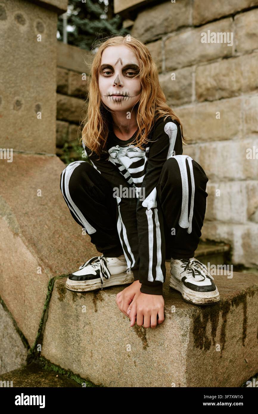 Ritratto di un bambino in costume da scheletro accovacciato all'aperto ad Halloween Foto Stock