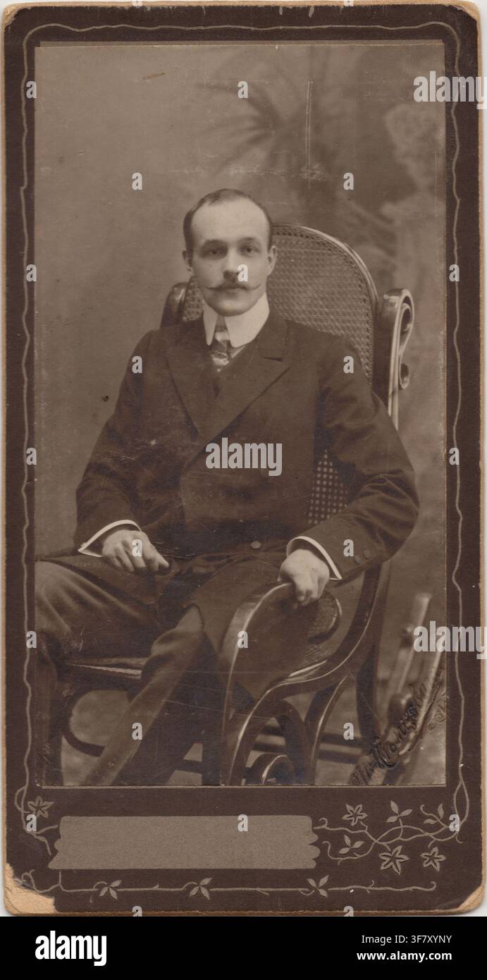 Un ritratto d'archivio in studio di un giovane elegante con i baffi, seduto su una sedia a dondolo in vimini, che indossa un completo vintage a tre pezzi wit Foto Stock
