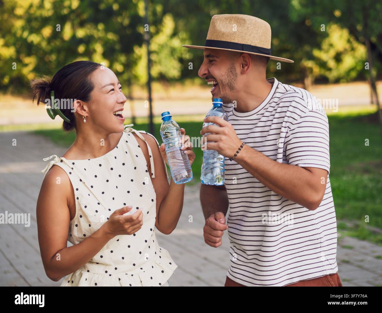 Una giovane coppia beve acqua nel parco in una giornata d'estate soleggiata. Foto Stock